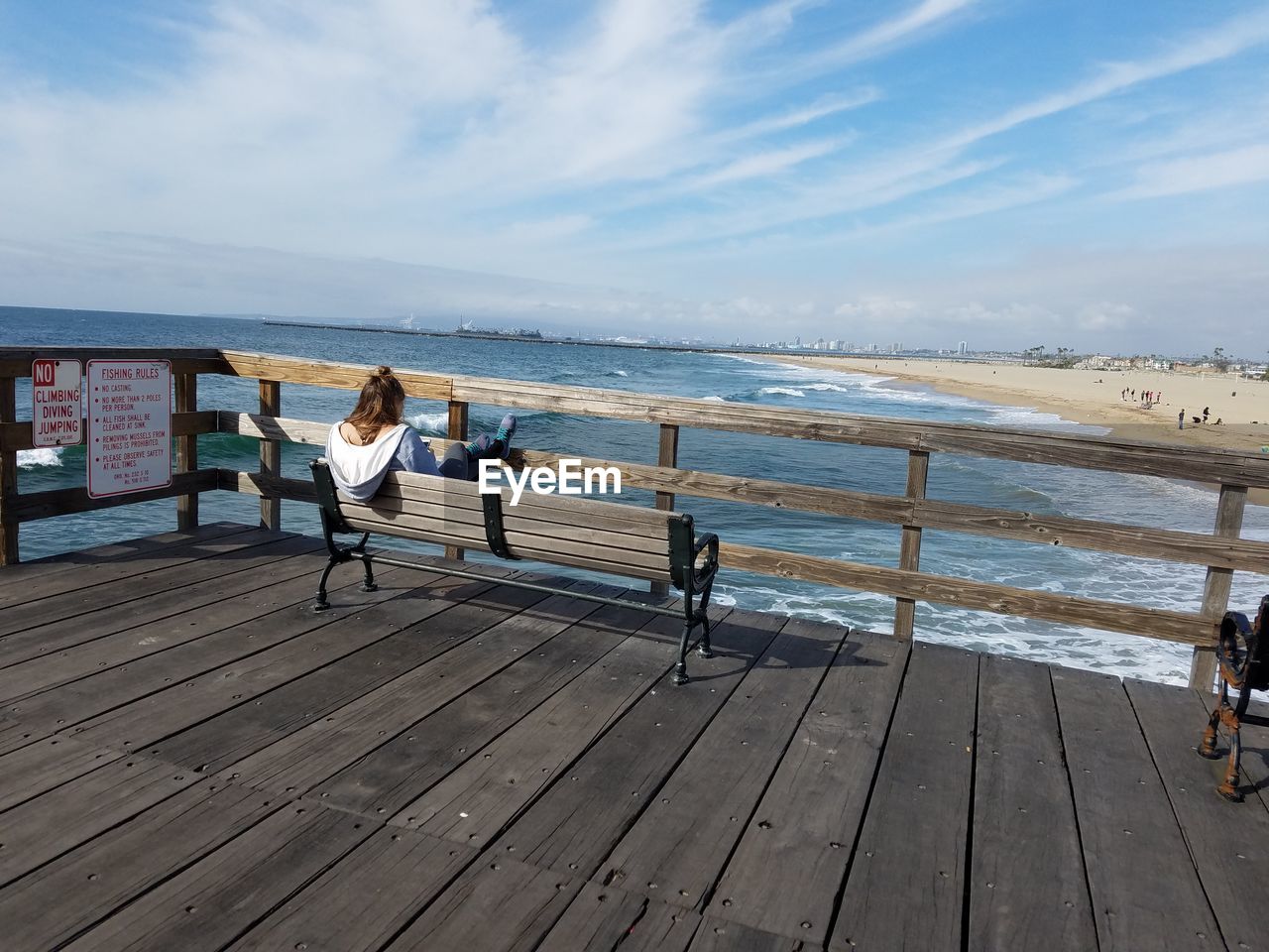 Rear view of woman sitting on bench at pier over sea against sky