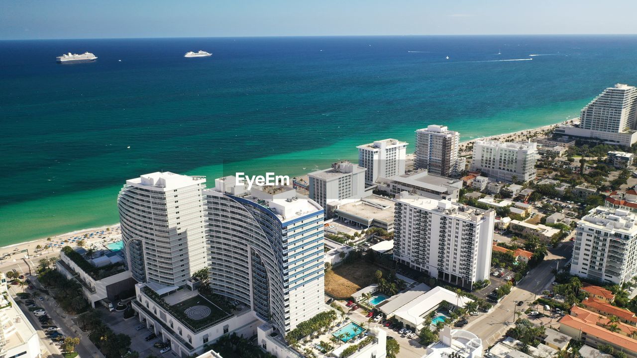 HIGH ANGLE VIEW OF SEA BY BUILDINGS AGAINST SKY