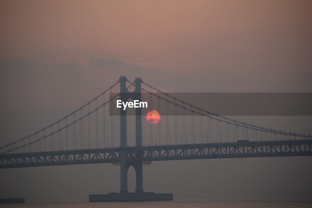 Suspension bridge over river against sky during sunset