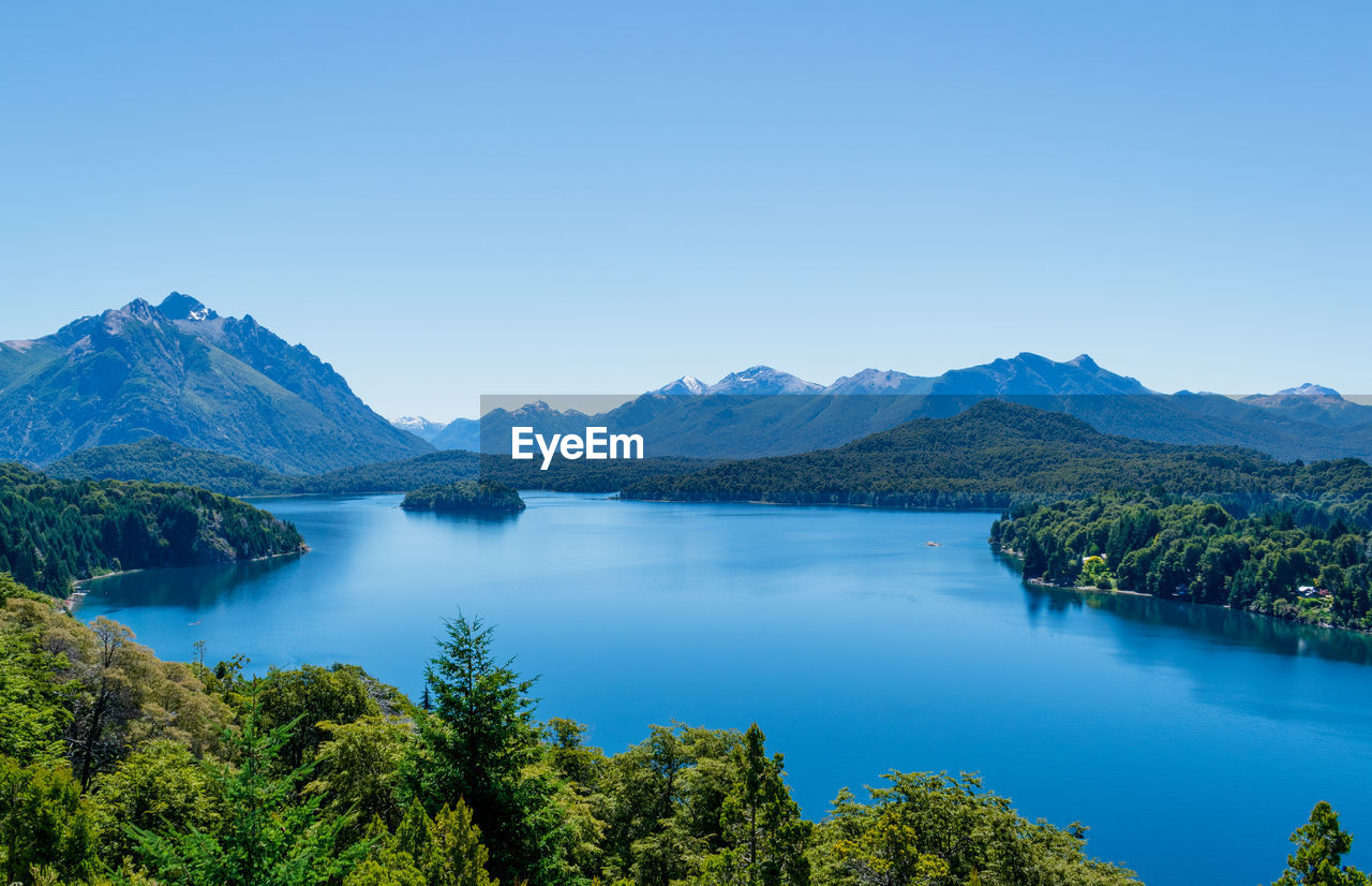 Scenic view of lake and mountains against clear blue sky