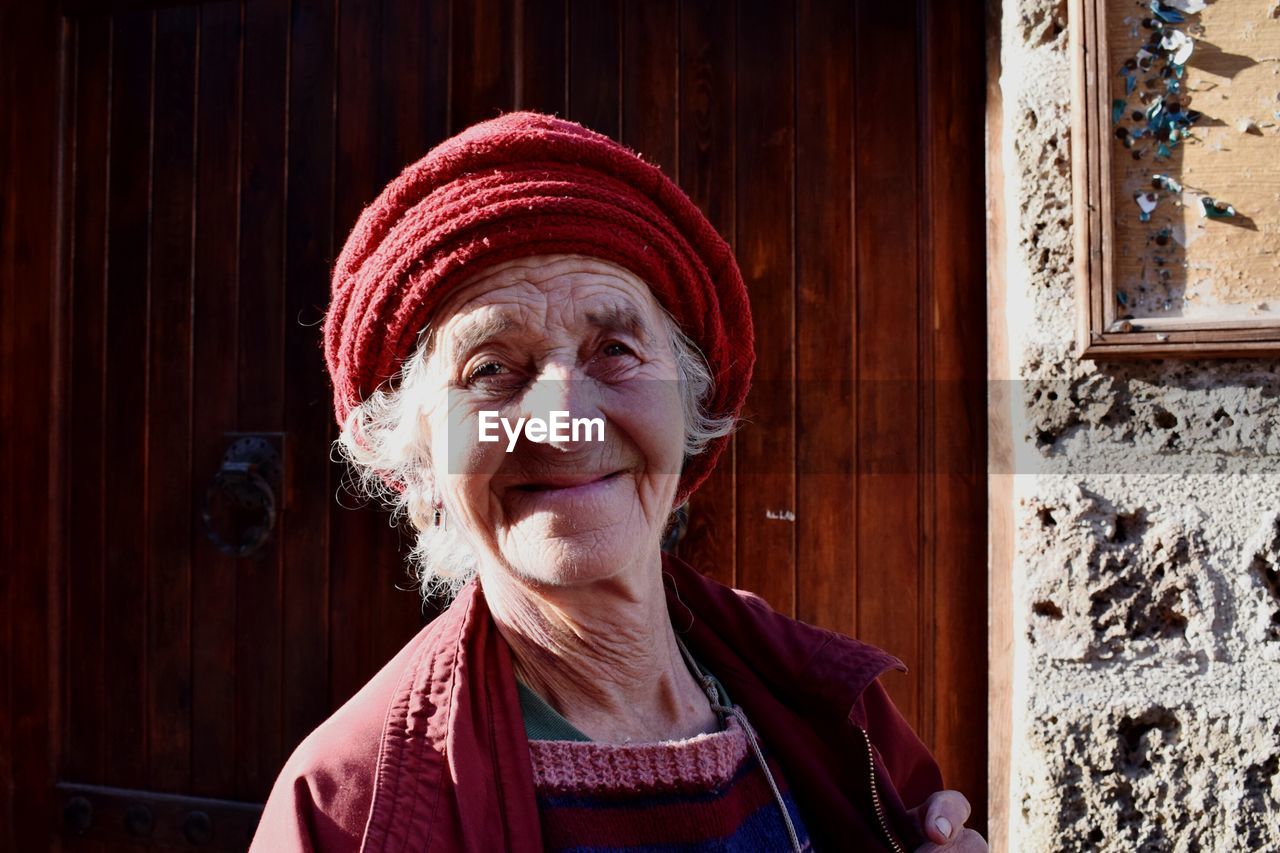 Portrait of smiling senior woman against door