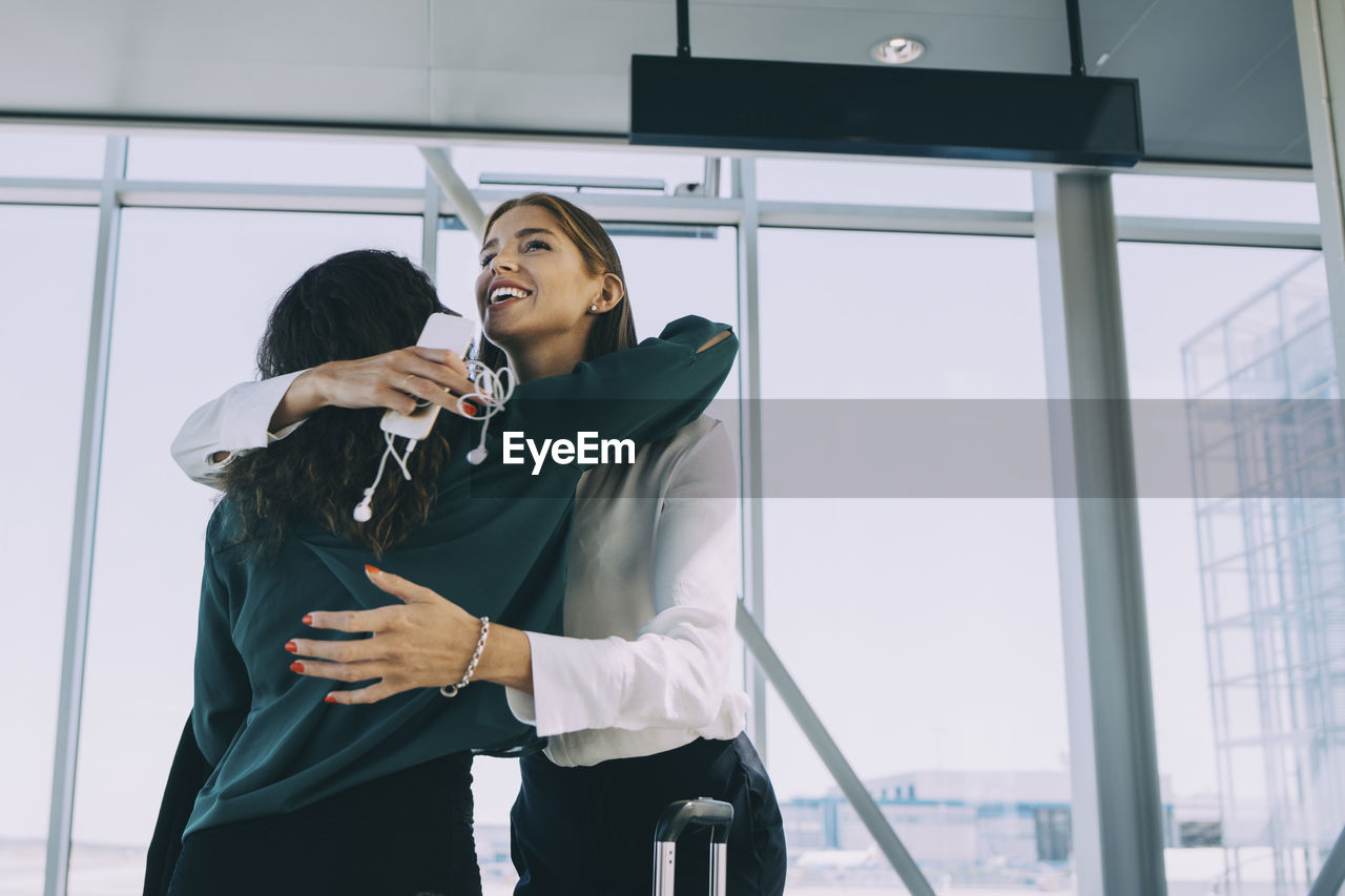 Low angle view of smiling businesswoman embracing colleague in corridor at airport