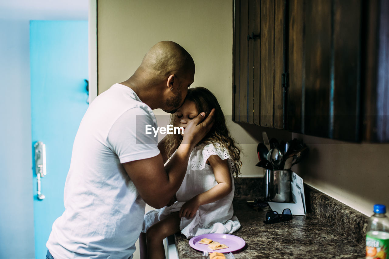 Dad kissing daughter while she sits on kitchen counter