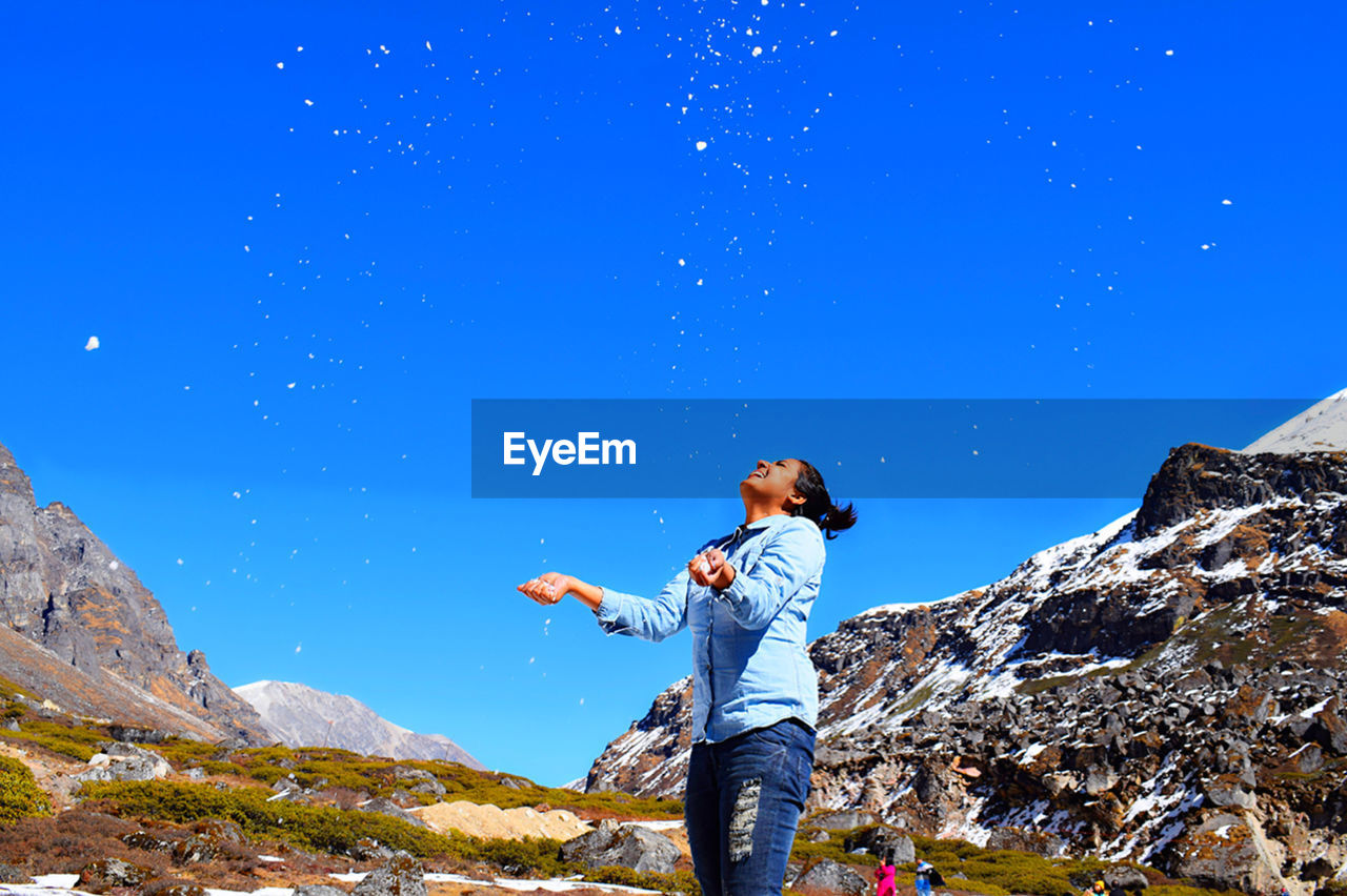 Full length of man standing on rock against blue sky