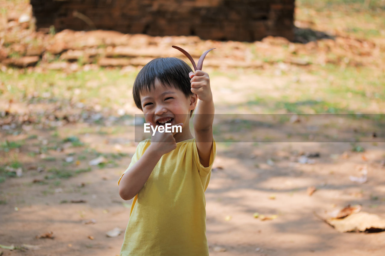 Happy boy holding leaves while standing outdoors