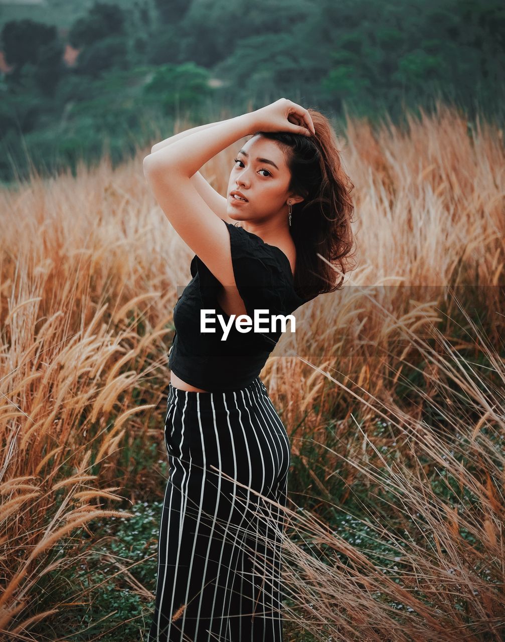 BEAUTIFUL YOUNG WOMAN LOOKING AWAY WHILE STANDING ON FIELD