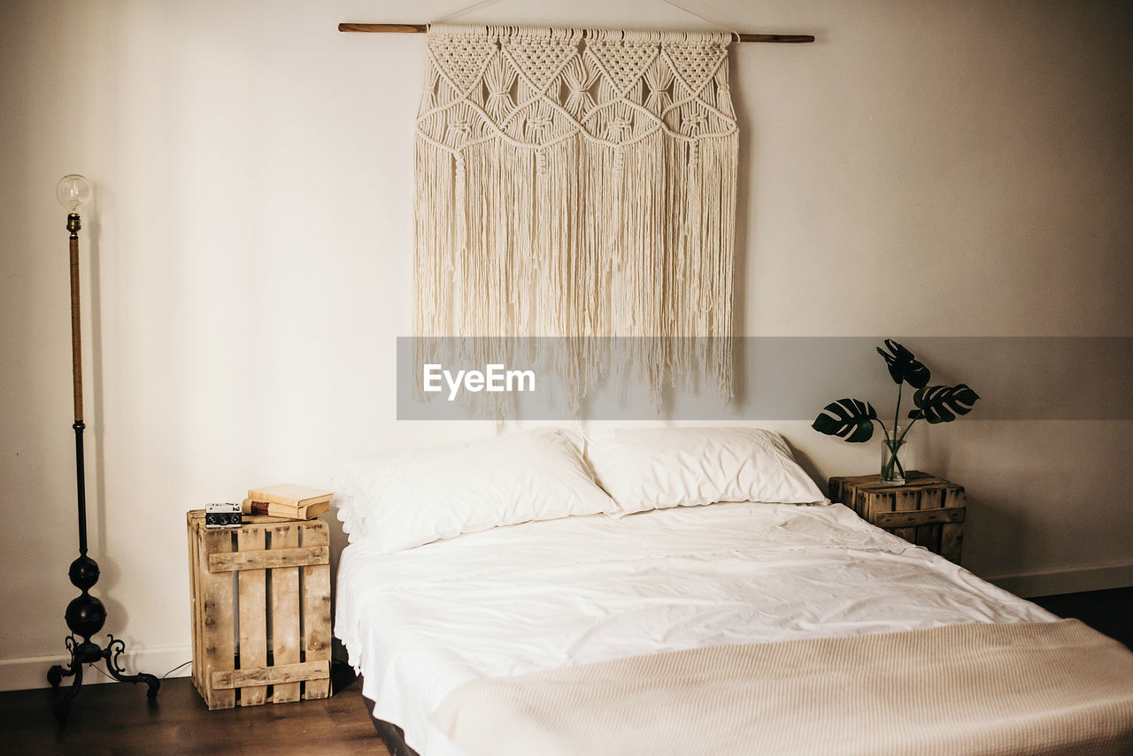 Vintage macrame decoration hanging on wall over comfortable bed in cozy bedroom at home