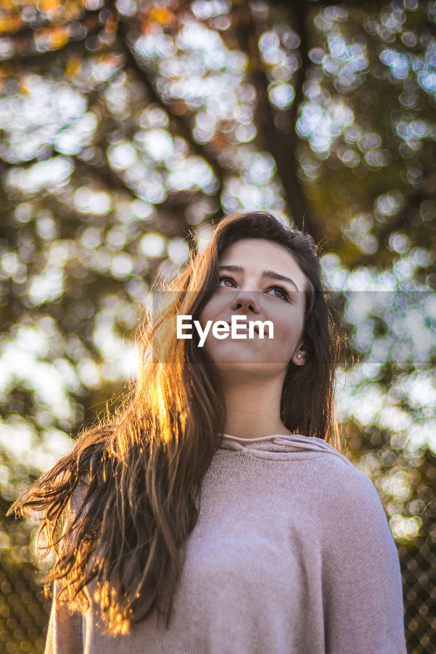 Portrait of young woman standing against tree