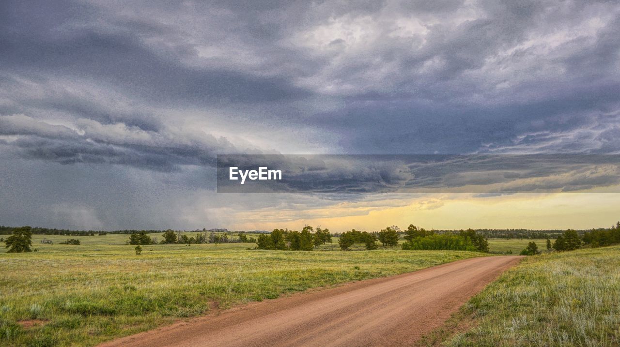 Dirt road amidst field against sky