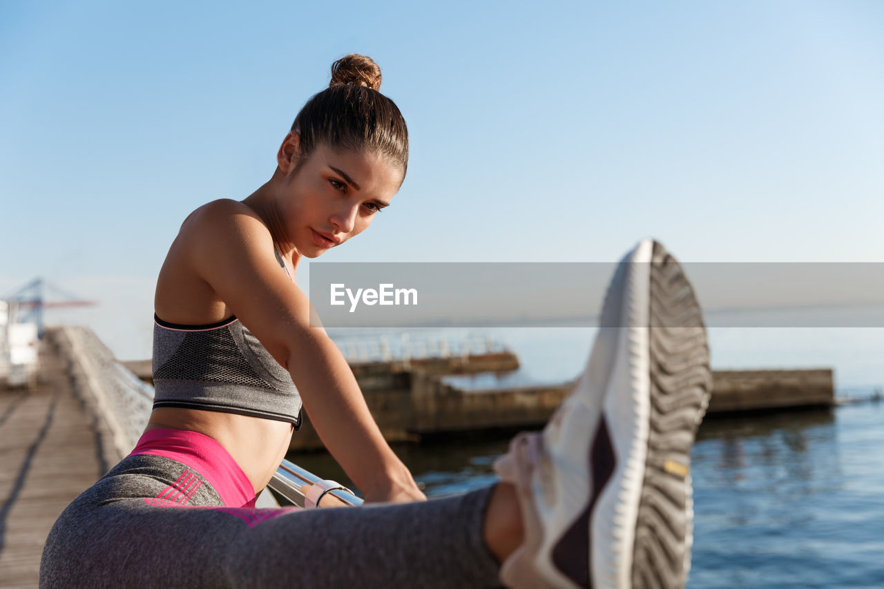 Woman sitting by sea against clear sky