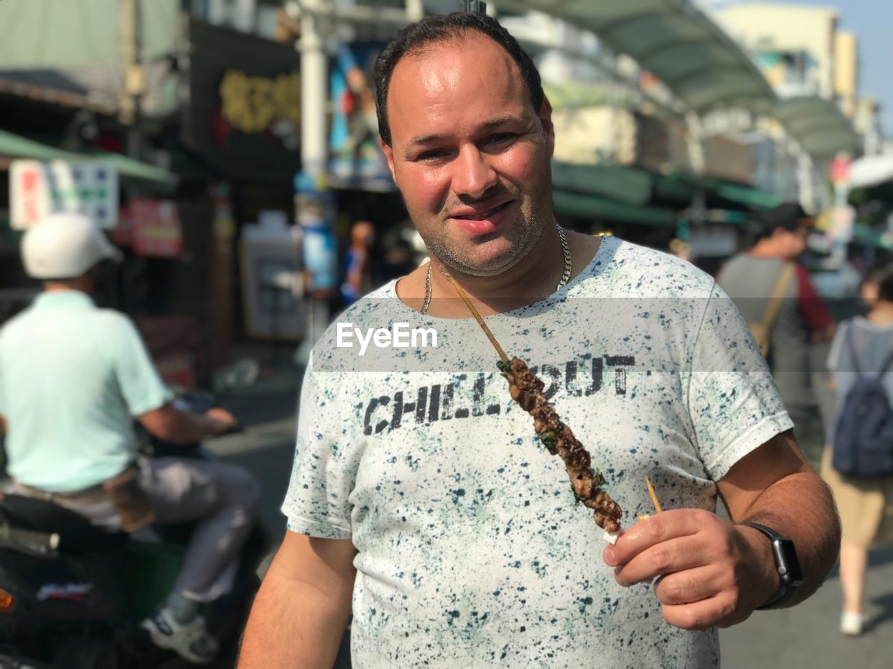 Portrait of mid adult man eating while standing on street in city