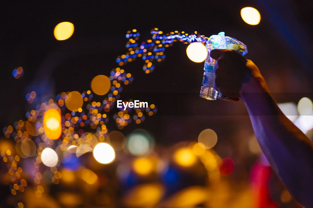 Close-up of man holding glass against illuminated street