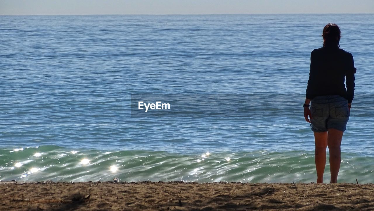 REAR VIEW OF WOMAN STANDING ON BEACH