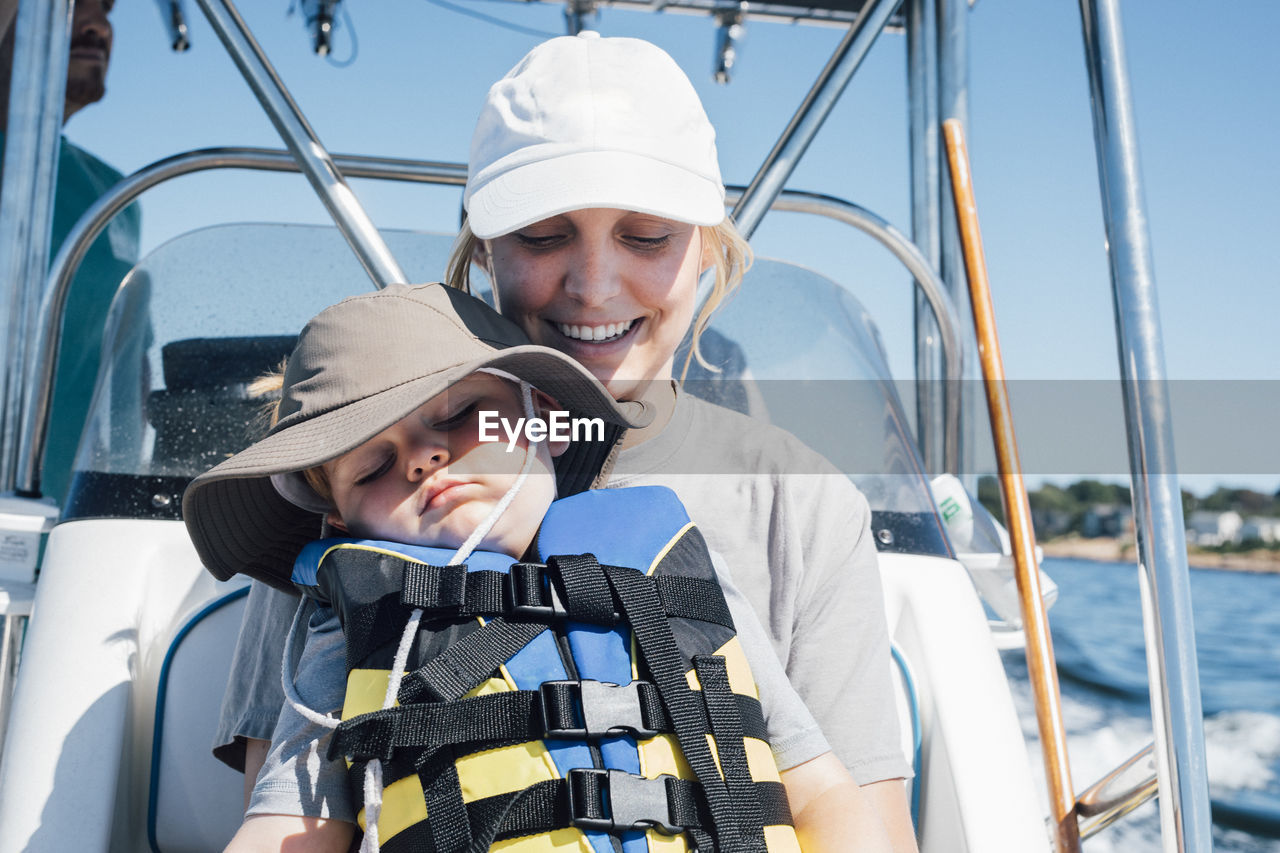 Smiling mother with son wearing life jacket in speedboat on sunny day