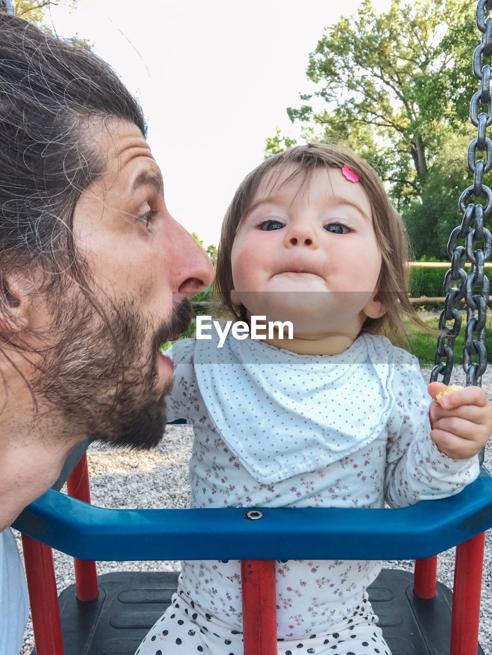 Close-up of man with cute toddler daughter on swing at playground