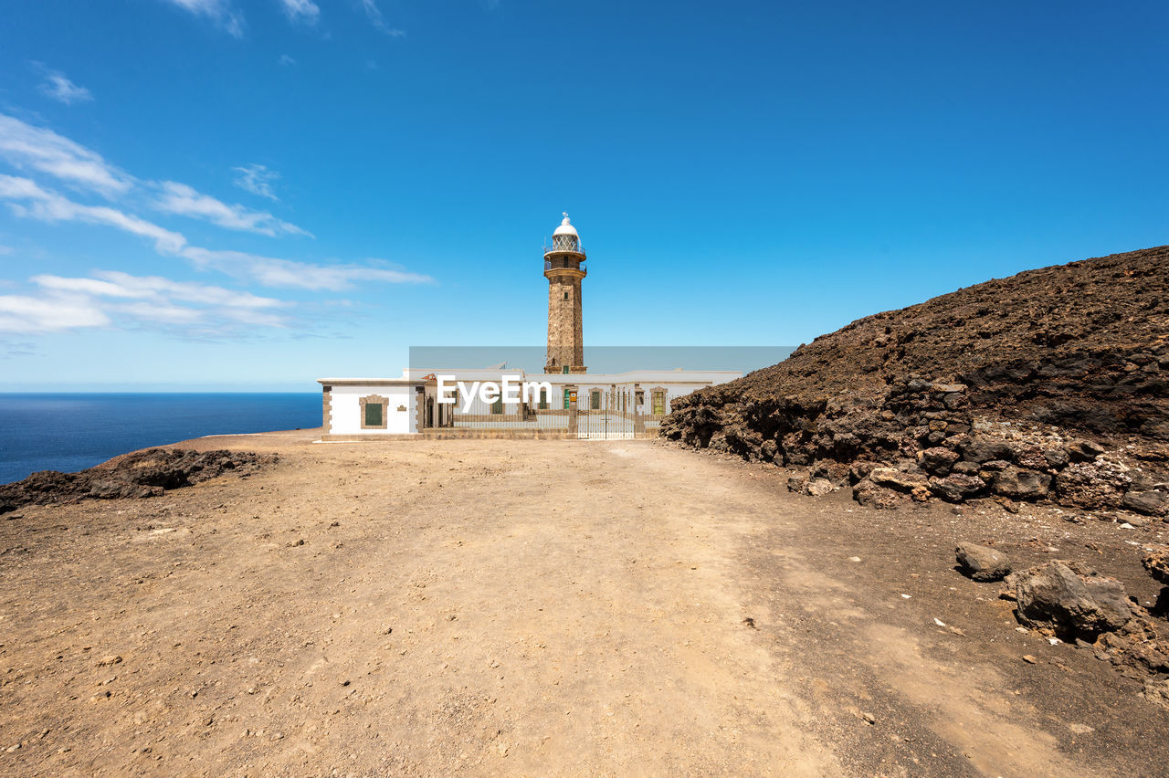 LIGHTHOUSE AMIDST BUILDINGS AGAINST SKY