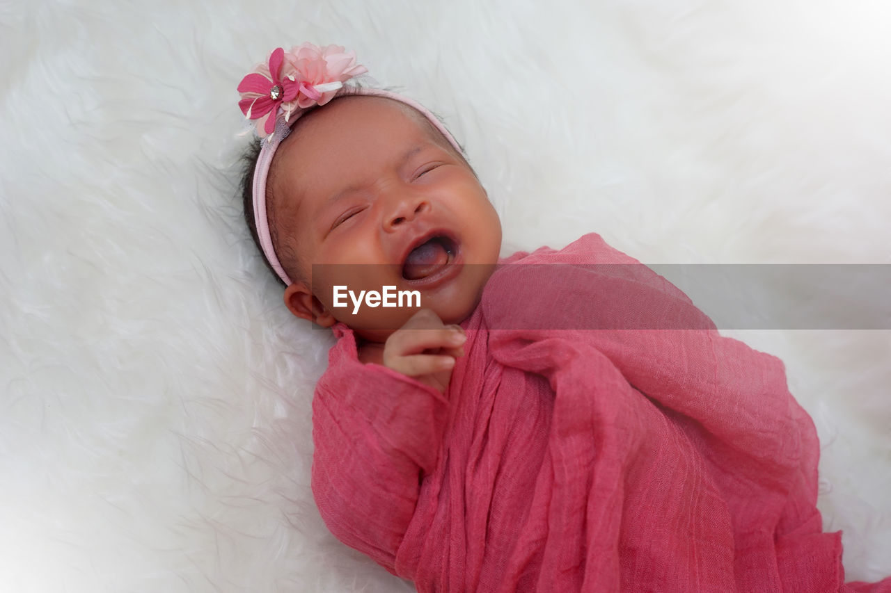 High angle view of baby girl in scarf crying while lying on bed