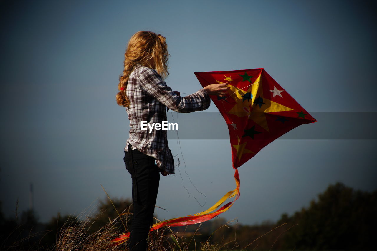 Woman holding kite while standing on field