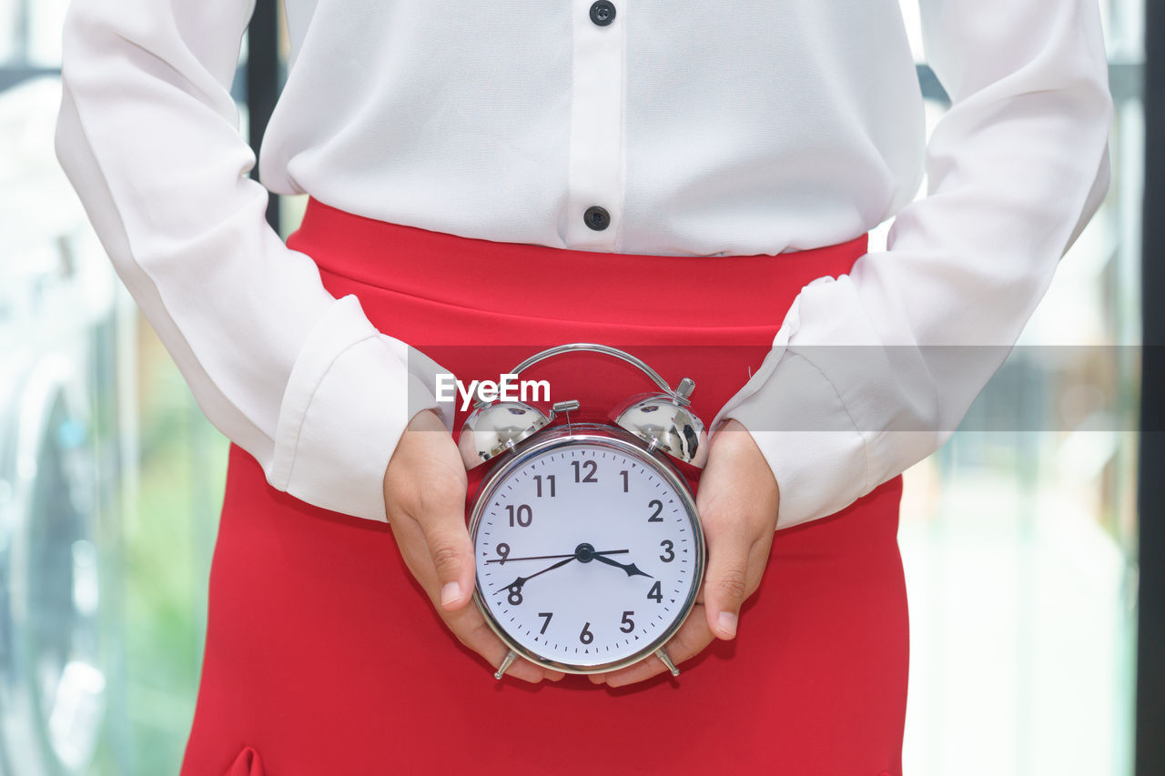 Midsection of businesswoman holding alarm clock