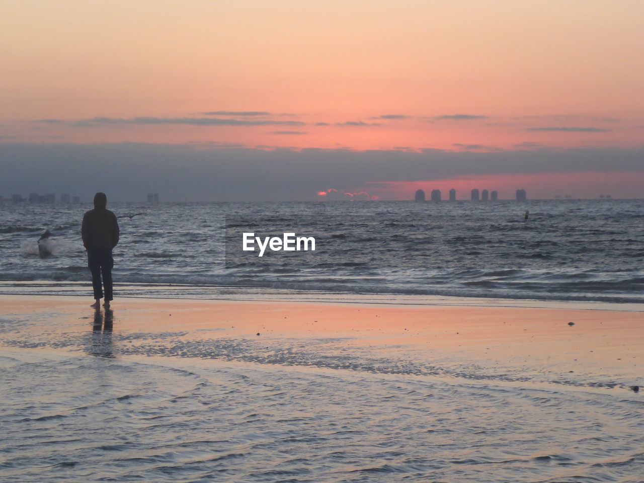 Silhouette man walking on shore at beach against sky during sunset