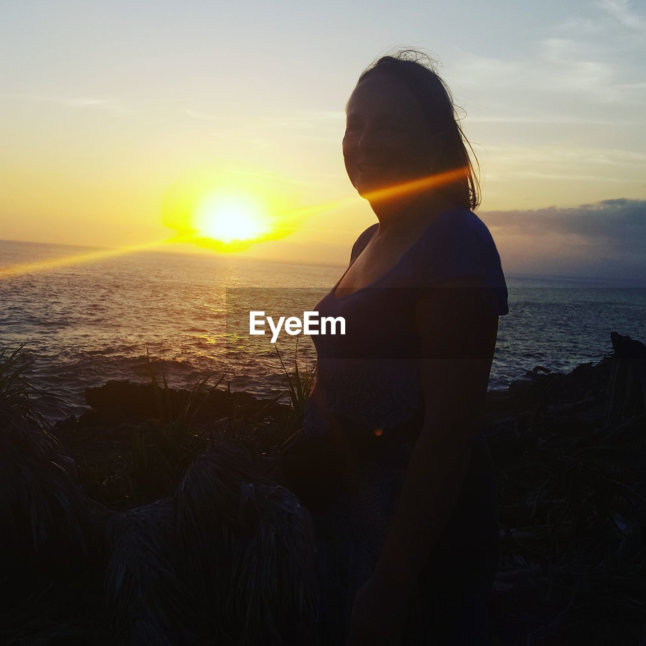 WOMAN STANDING ON BEACH DURING SUNSET