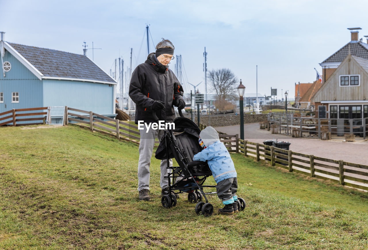 Grandfather and granddaughter with baby stroller on field in town