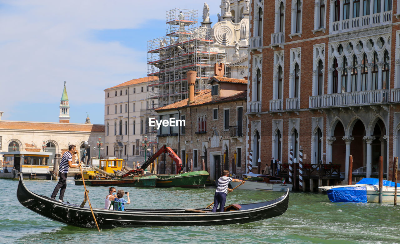 PEOPLE ON BOAT IN CANAL AGAINST BUILDINGS