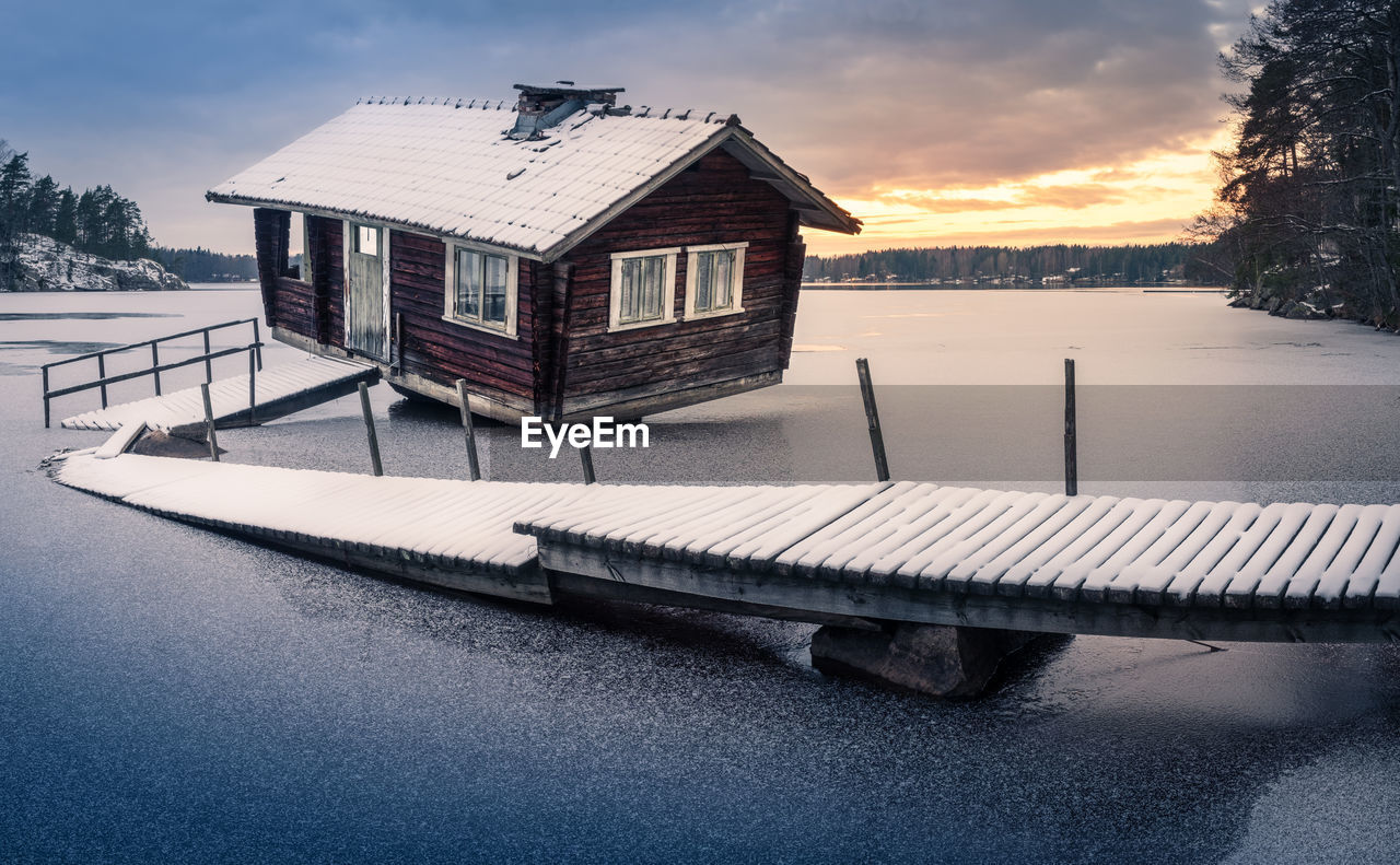 Sauna cottage by lake against sky during sunset with pier