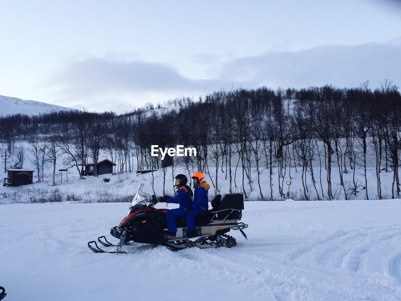 Side view of friends snowmobiling on snowy field against sky