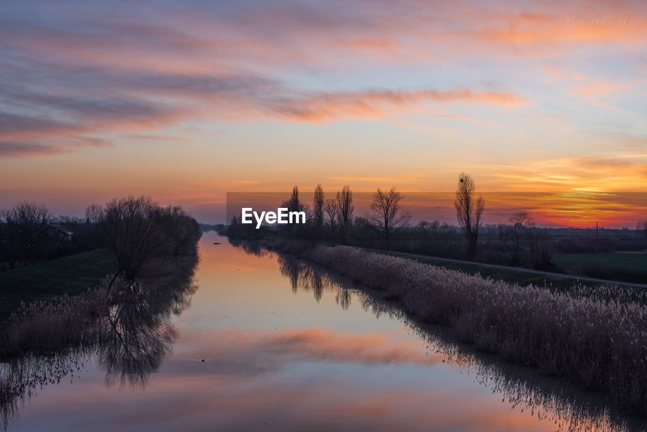 sky, sunset, reflection, dawn, beauty in nature, scenics - nature, water, tranquility, cloud, landscape, evening, plant, nature, tranquil scene, environment, tree, river, no people, orange color, land, sun, rural scene, idyllic, twilight, non-urban scene, dramatic sky, horizon, outdoors, afterglow, agriculture, field, silhouette, travel destinations, growth, marsh