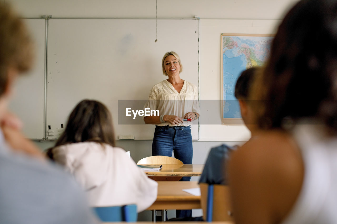 Smiling female professor teaching students in classroom at high school