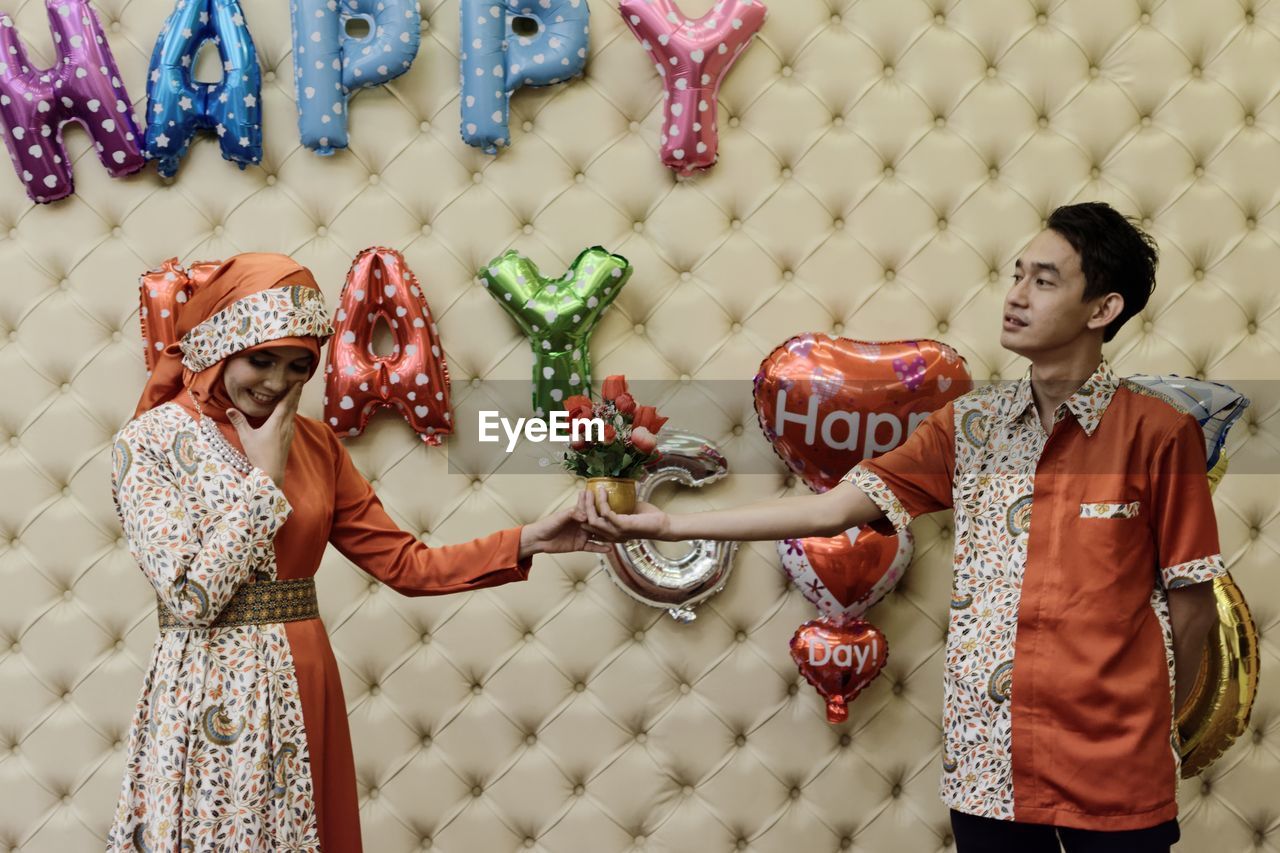 Couple holding flowers while standing against decoration at home