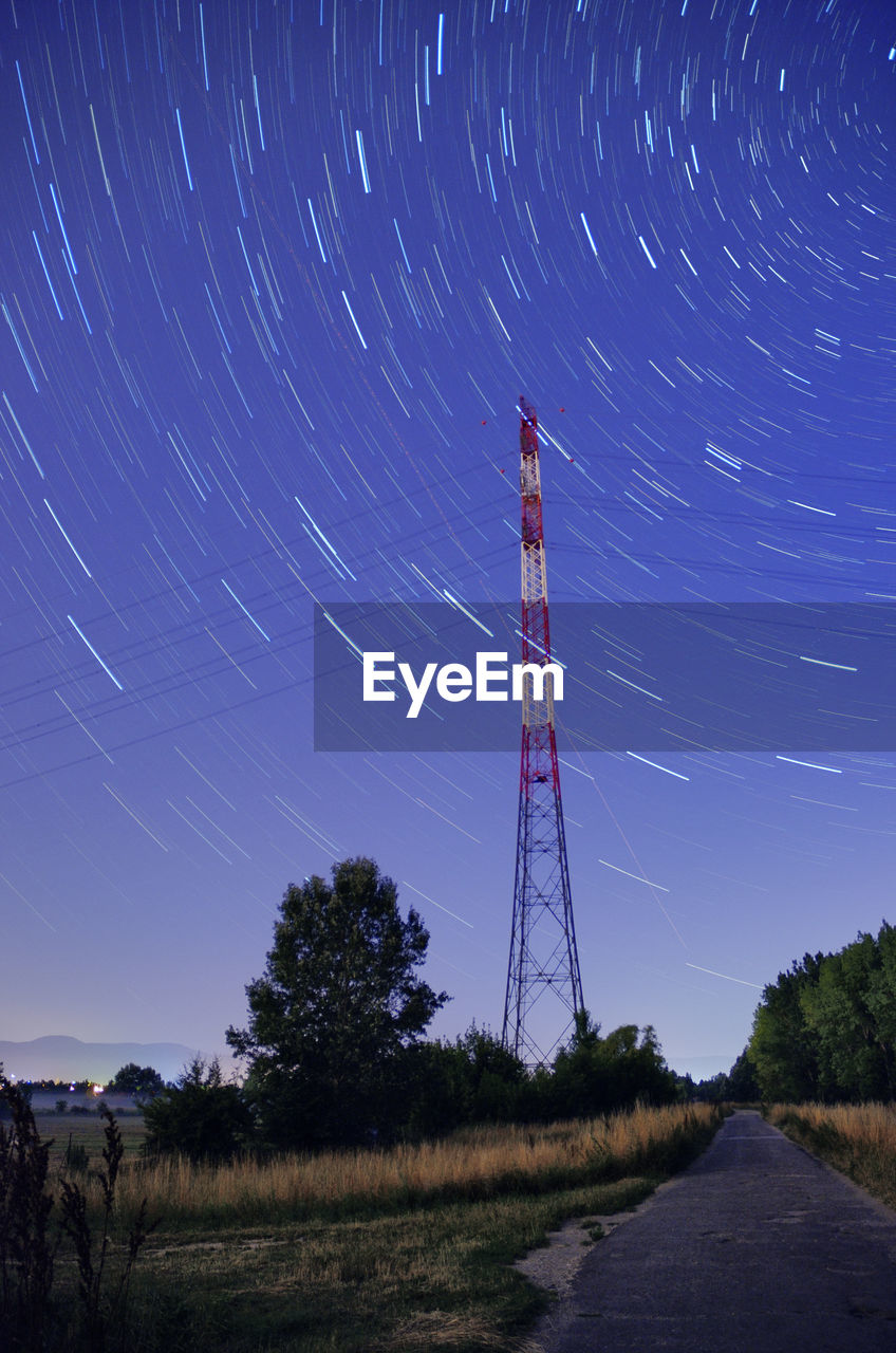 Low angle view of electricity pylon against star trail at night