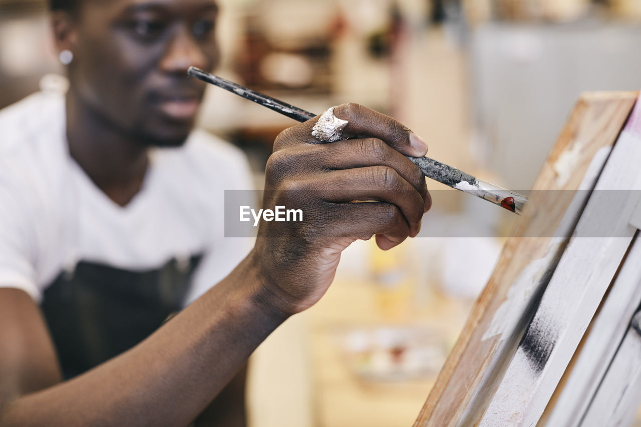 Young man painting with paintbrush on canvas in art class