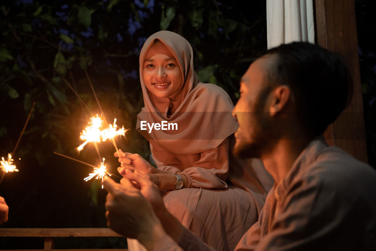 Happy couple holding sparkler at night