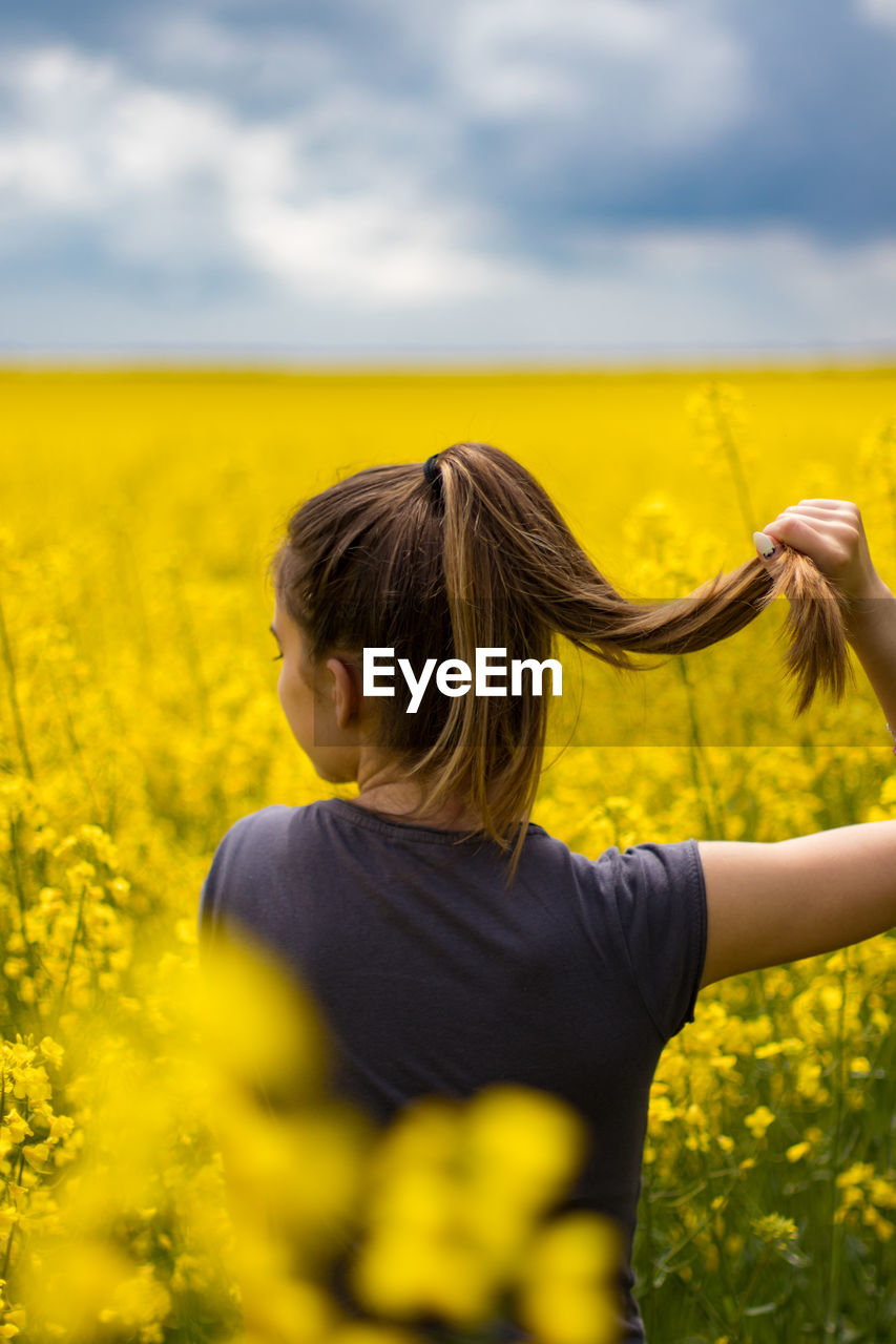 REAR VIEW OF WOMAN WITH YELLOW FLOWERS ON FIELD