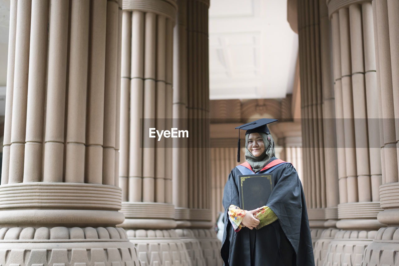 Portrait of smiling young woman wearing graduation gown at university