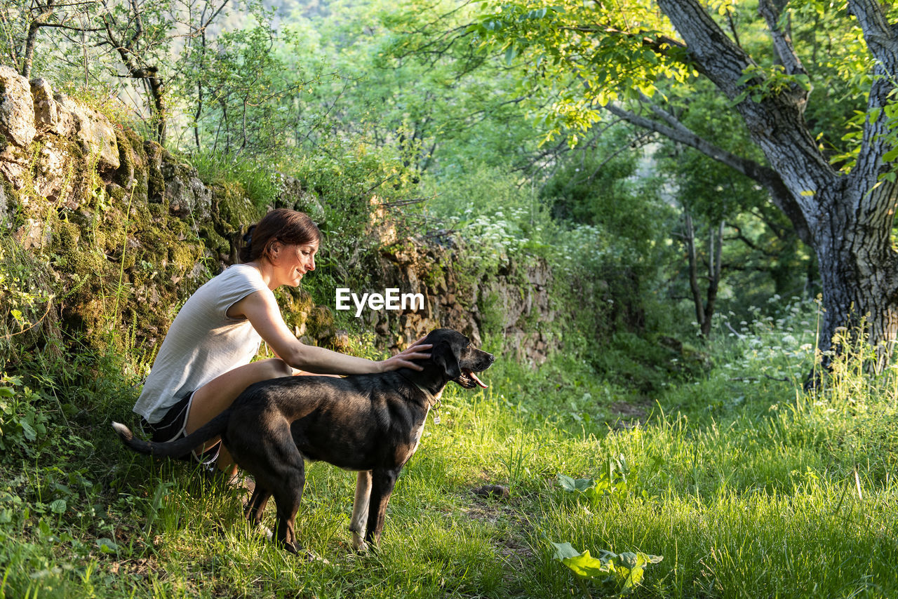 Woman petting and playing with her dog in a forest.