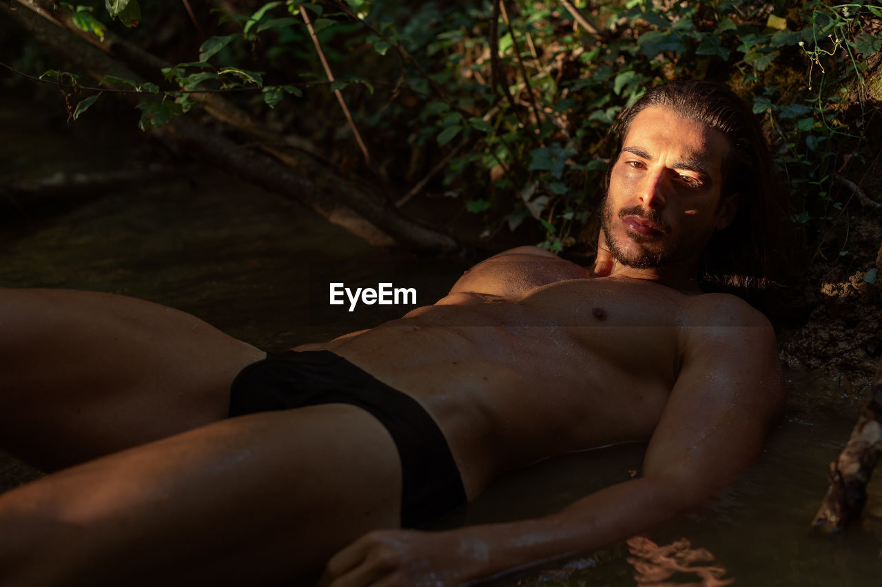 Portrait of shirtless young man lying in lake