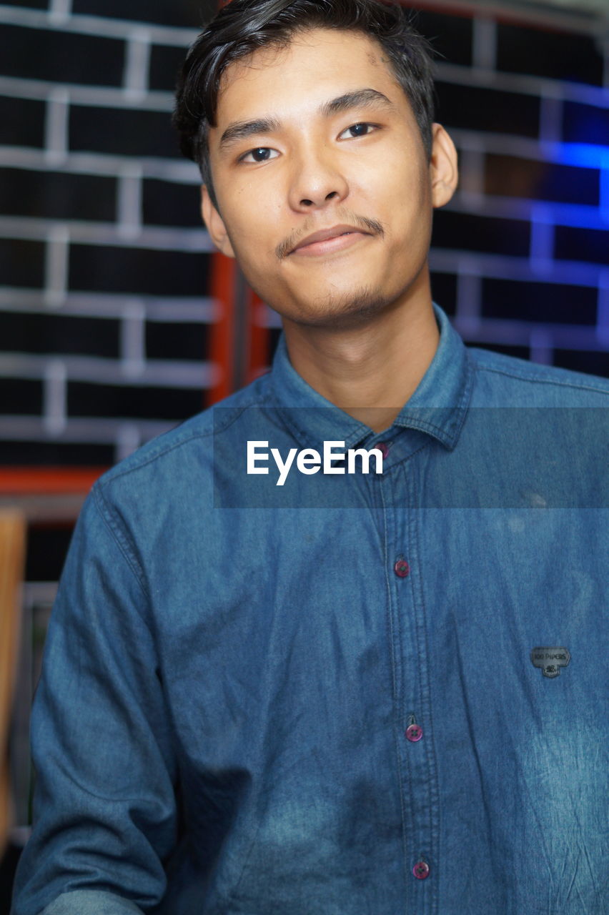 PORTRAIT OF SMILING YOUNG MAN STANDING AGAINST BLUE WALL