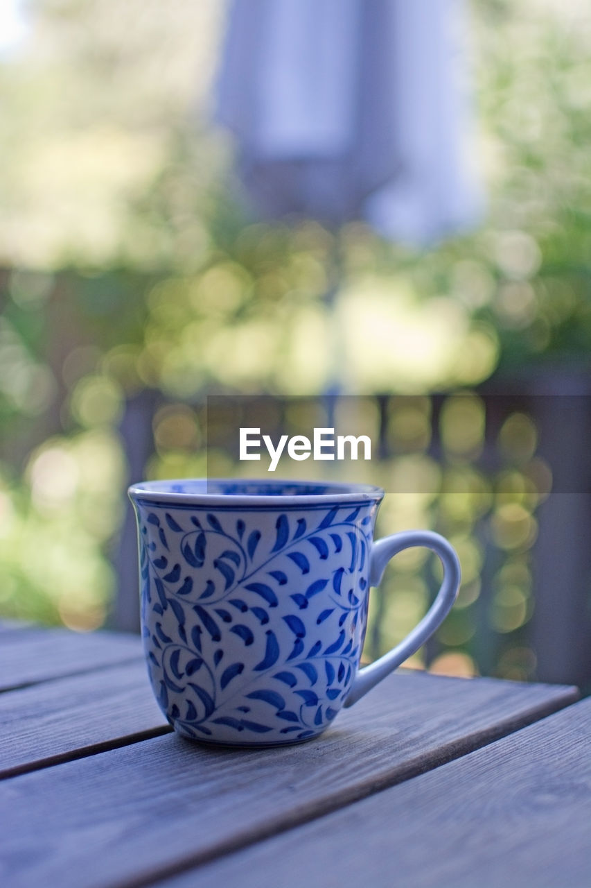 CLOSE-UP OF COFFEE CUP ON TABLE AGAINST BLURRED BACKGROUND
