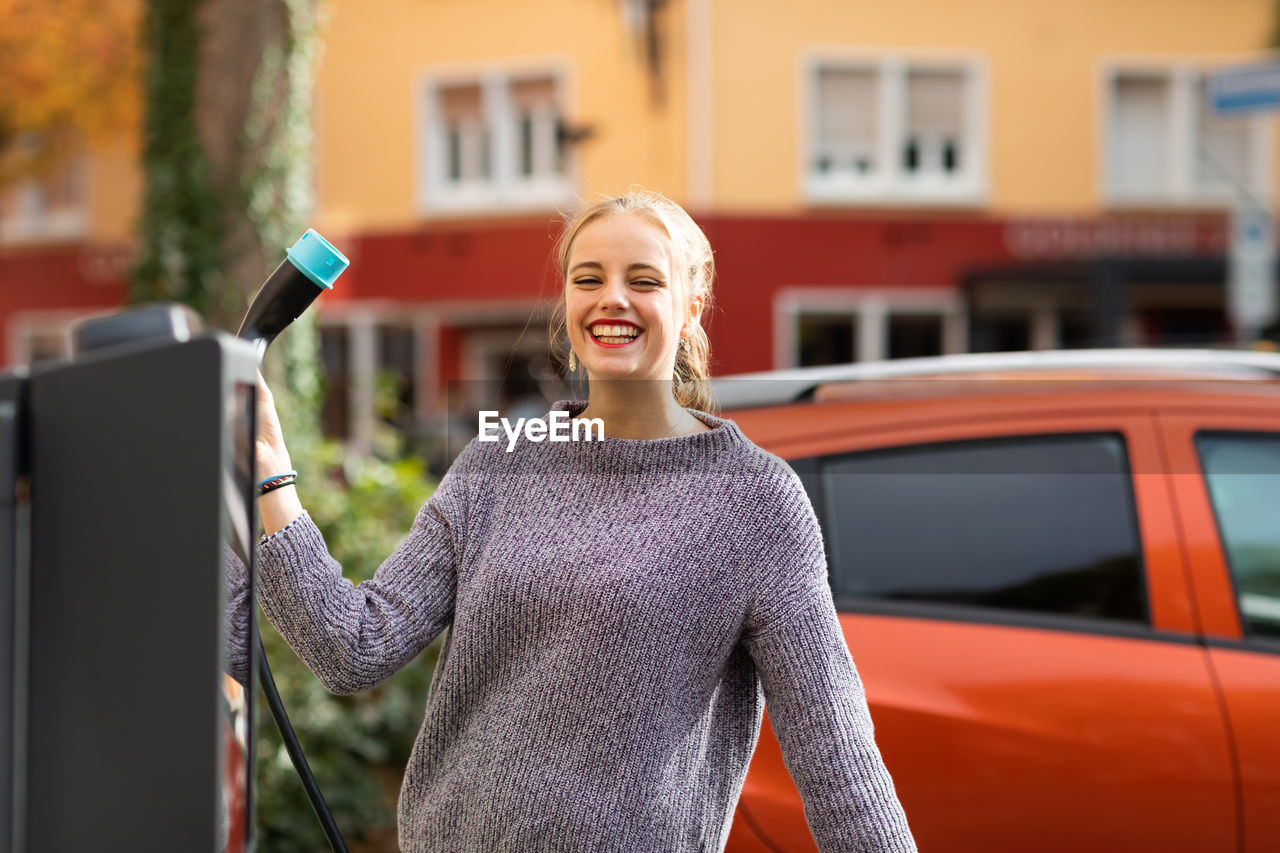 Young woman using an electric charging station with a car