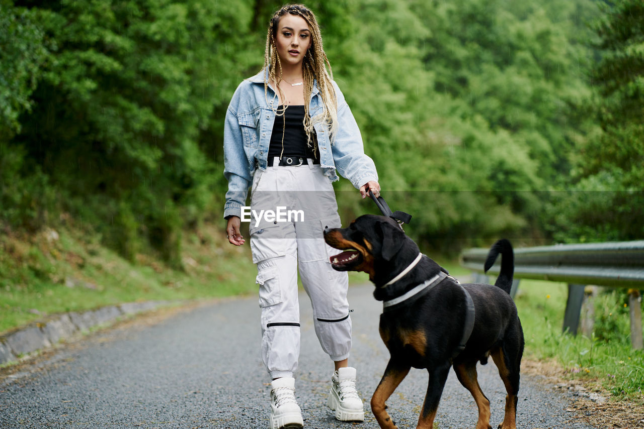 Young woman with blonde braided hair wearing a denim jacket and white jean walking her dog on a rainy day