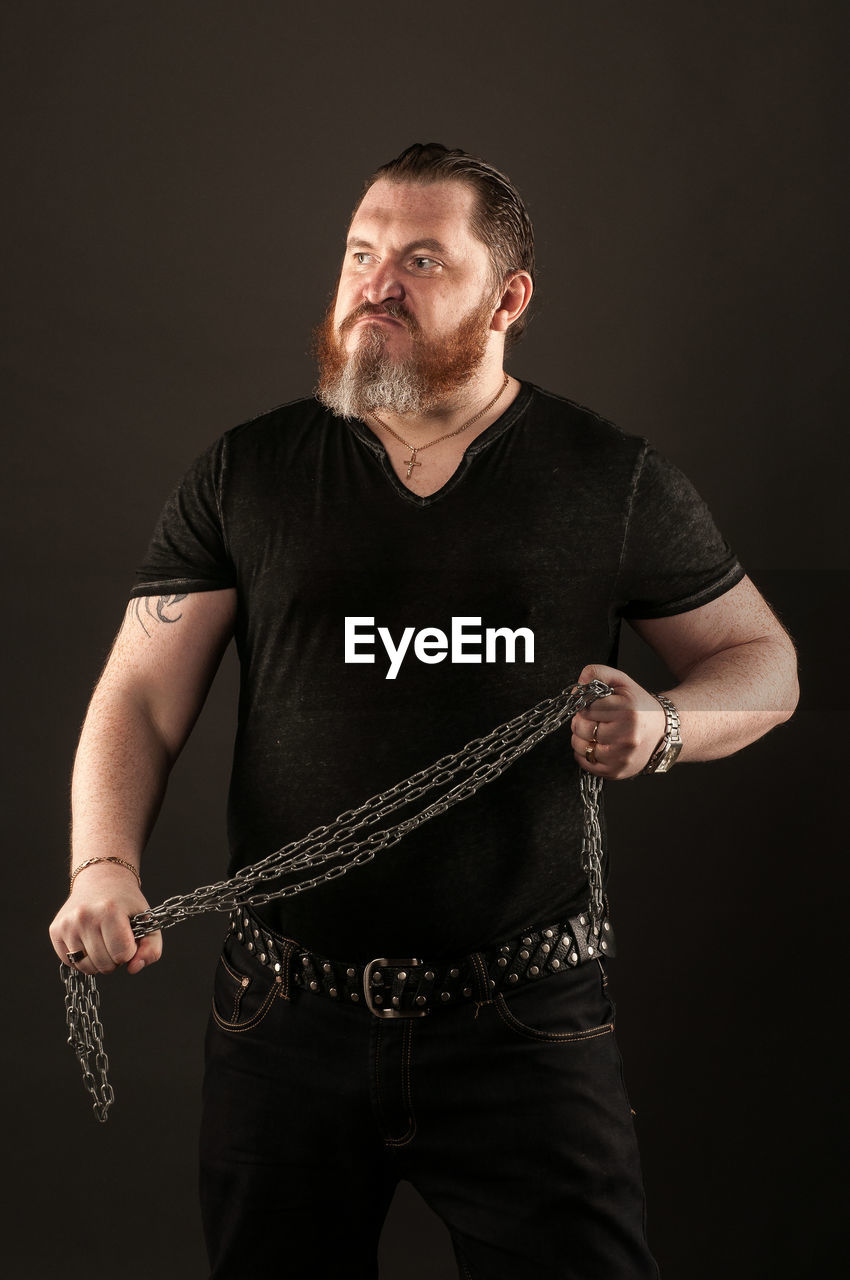 Aggressive man holding chain against black background