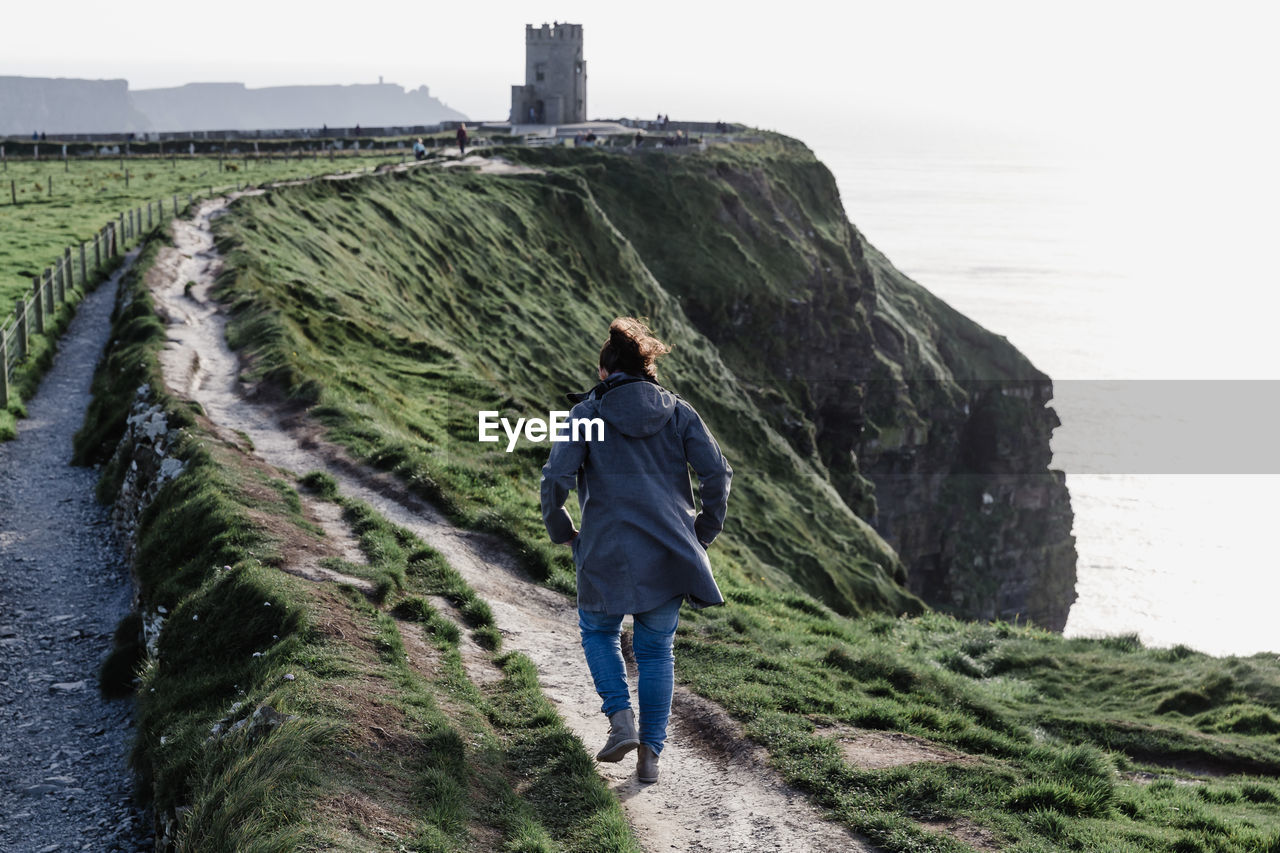 Rear view of young woman walking on mountain by sea against sky