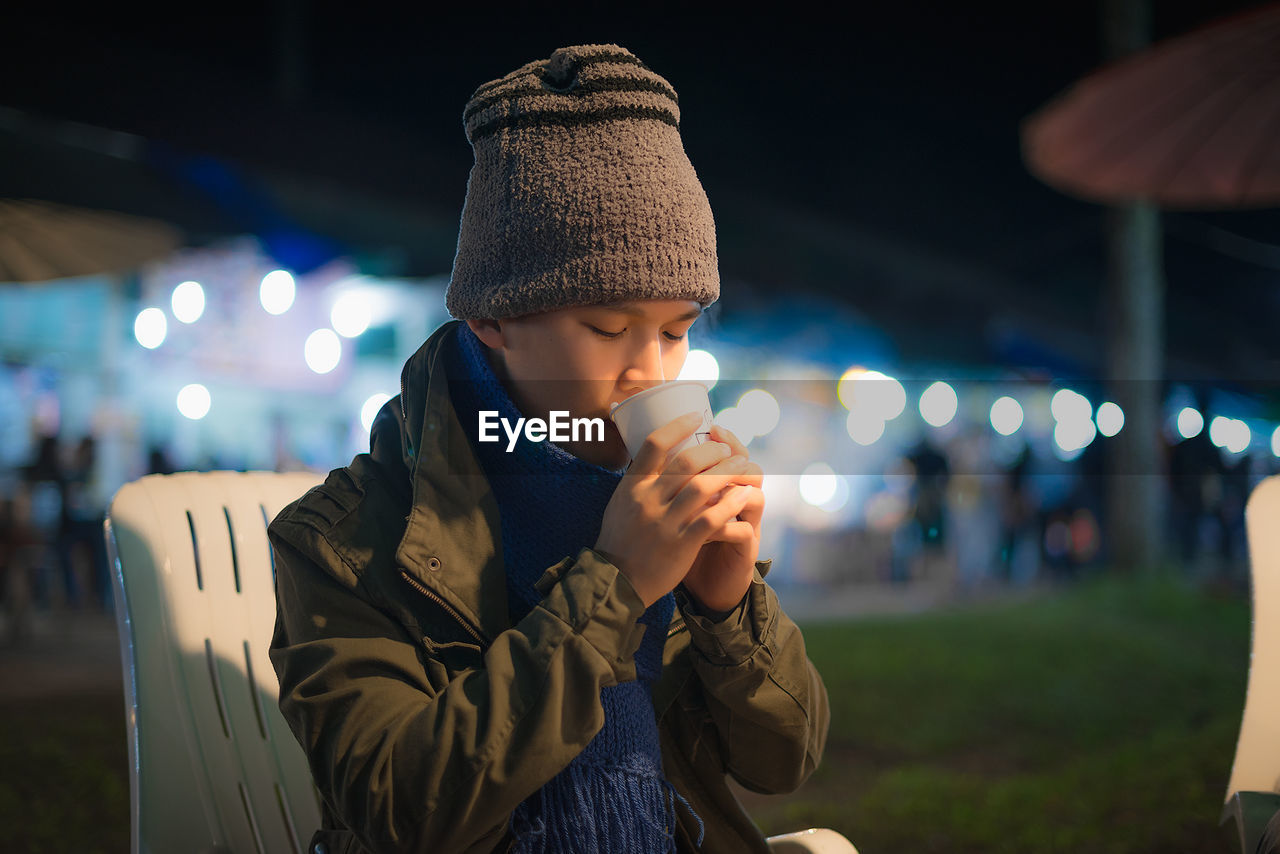 Man wearing warm clothing while drinking coffee at night