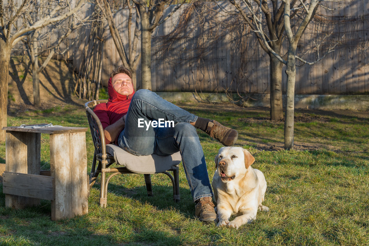 Adult man relaxes alone in the yard with trees and green grass d