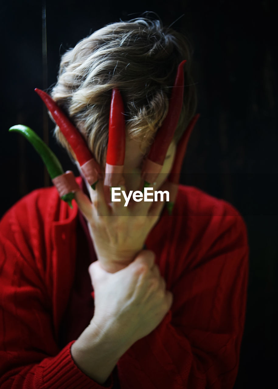 PORTRAIT OF WOMAN COVERING FACE WITH HAND ON RED BACKGROUND