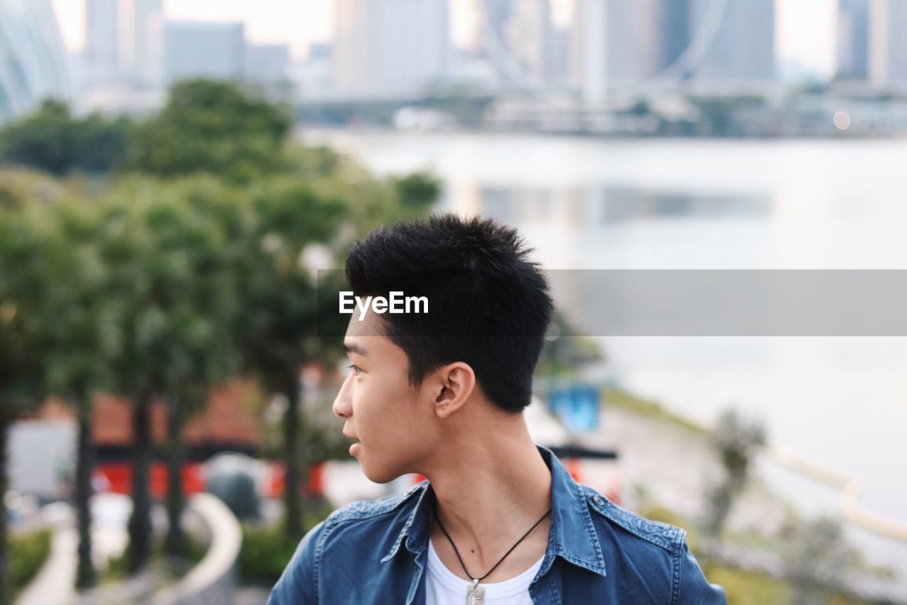 Young man looking away while standing against river