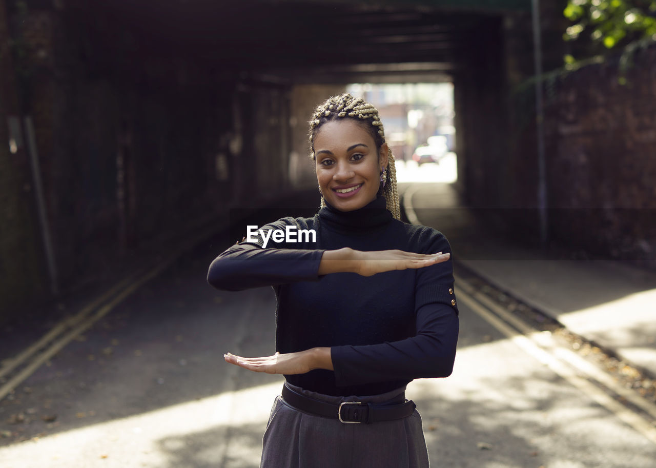 Portrait of woman gesturing while standing on footpath against buildings